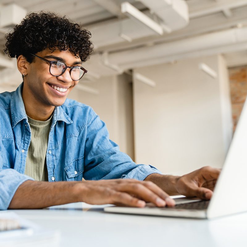 Happy smiling afro businessman using laptop at the desk in office